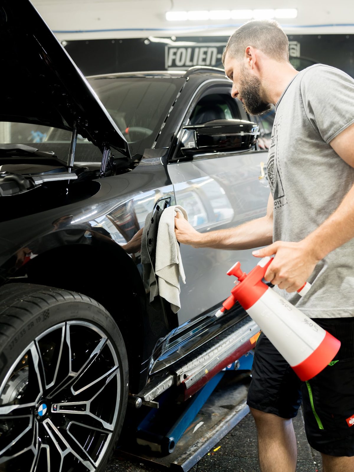 Ein Mitarbeiter sprüht Reiniger auf den Kotflügel eines schwarzen Autos und wischt nach